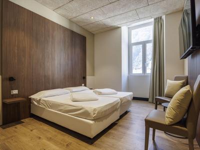 Modern eingerichtetes Hotelzimmer mit Doppelbett, Holzfußboden und einem Fenster mit Vorhängen.
