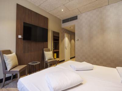 Modernes Hotelzimmer mit Doppelbett, Wandfernseher und zwei Stühlen neben einem kleinen Tisch.