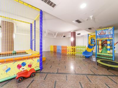 Helle, farbenfrohe Kinderspielzone mit Trampolin, Rutsche und Spielnetz in einem großen Innenraum.