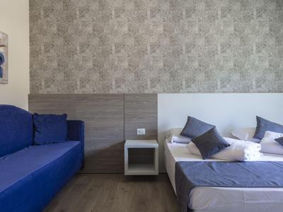 Modernes Hotelzimmer mit Doppelbett, blauer Couch und minimalistischem Nachttisch.