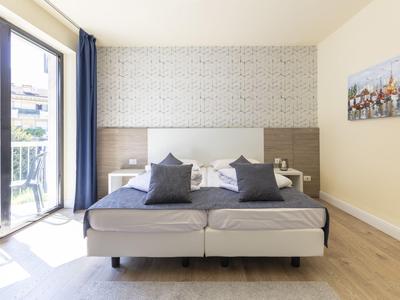 Modernes Hotelzimmer mit zwei Betten, grauen Kissen und Balkon mit Stadtblick.