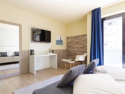 Helles Hotelzimmer mit Doppelbett, Fenster, TV und Schreibtisch mit Stuhl.
