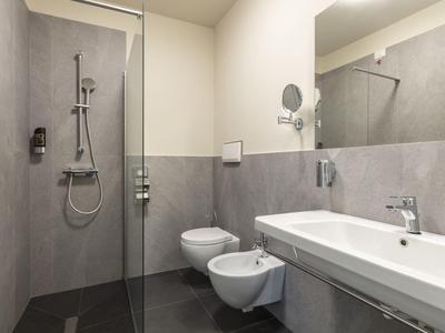 Moderner Hotelbadezimmer mit Dusche, WC, Bidet und Waschbecken in neutralen Grautönen.