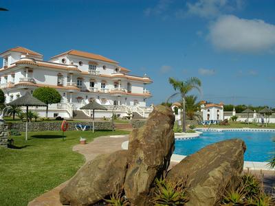 Hotel de lujo con piscina, palmeras y césped verde bajo cielo azul.