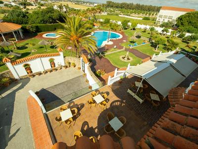 Vista de un área de hotel de lujo con piscina, jardín y zonas de descanso bajo un clima soleado.