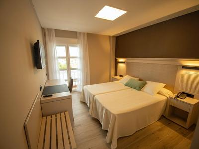 Nowoczesny pokój hotelowy z dwoma pojedynczymi łóżkami, jasnymi ścianami i balkonem z naturalnym światłem.