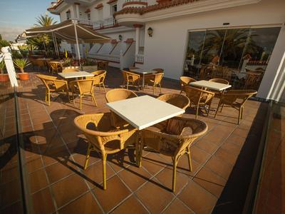 Terraza con mesas y sillas frente a un edificio de hotel bajo la luz del sol.
