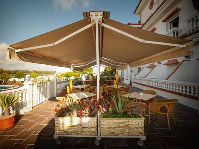 Terraza con macetas y sombrilla frente a un edificio de hotel al atardecer.
