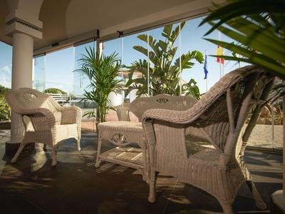 Terraza soleada con sillas de mimbre y plantas verdes bajo un toldo.