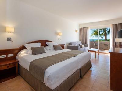 Gemütliches Hotelzimmer mit großen Betten, Sitzbereich und Blick auf Palmen und Meer.