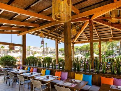 Offener, holzgetäfelter Außenbereich eines Restaurants mit bunten Kissen und modernen Tischen.