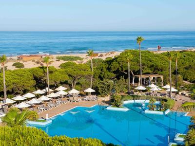 Großer Swimmingpool mit Liegestühlen und Sonnenschirmen neben Stränden und Meerblick.