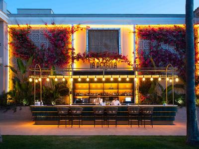 Abendaufnahme einer beleuchteten Open-Air-Bar mit dekorativem Pflanzenbewuchs an der Wand.