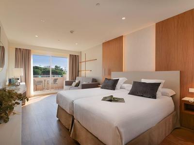 Modernes Hotelzimmer mit zwei Einzelbetten, Balkon und Blick auf Grünflächen.