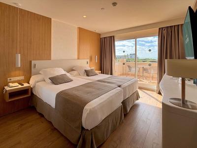 Helles Hotelzimmer mit zwei Betten, Holzboden und Zugang zu einem Balkon mit Ausblick.
