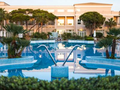 Luxuriöses Hotel mit großem Pool, umgeben von Palmen und Liegestühlen bei Dämmerung.