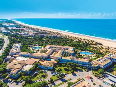 Luftaufnahme eines Strandhotels mit Pool, umgeben von Grünflächen und nah am Sandstrand.