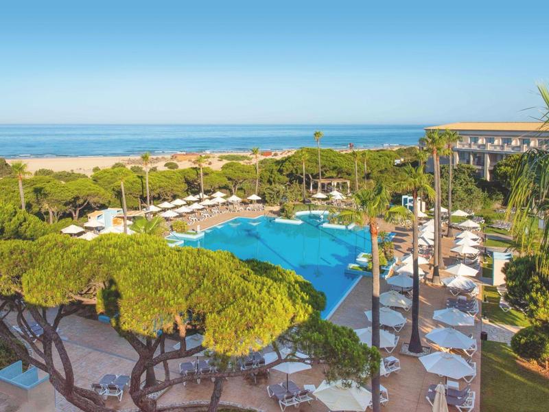 Großer Hotelpool mit Liegestühlen und Blick auf das Meer an einem sonnigen Tag.