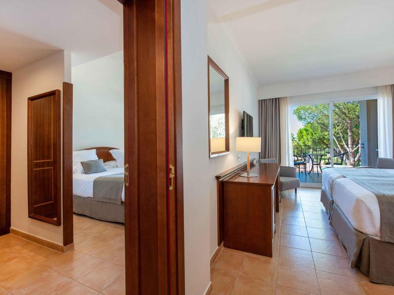 Hell eingerichtetes Hotelzimmer mit Zugang zu Balkon und Blick auf Grünfläche.