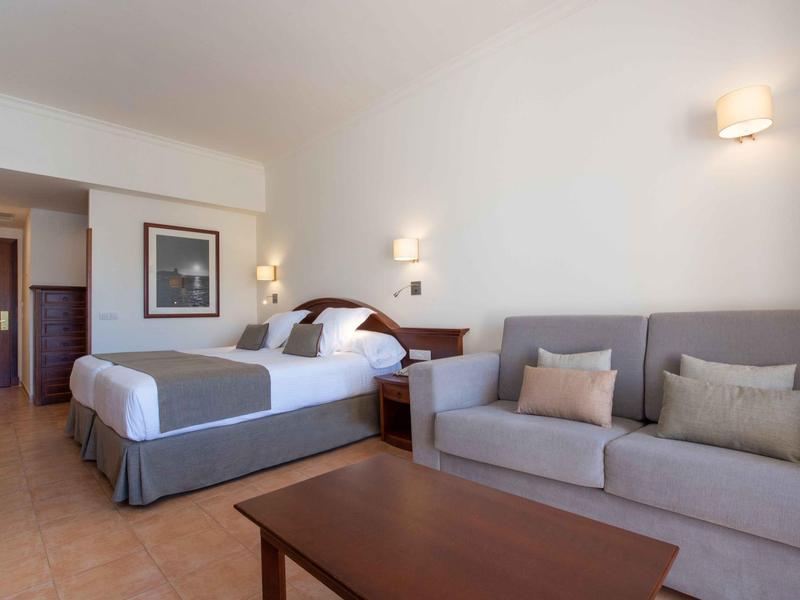 Modern eingerichtetes Hotelzimmer mit Doppelbett, Sofa und Holztisch.