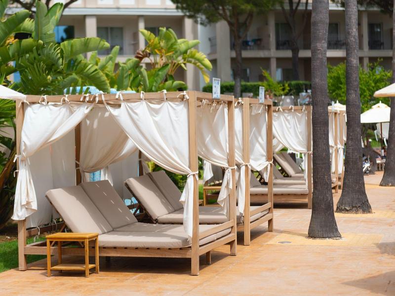 Reihe von weißen, mit Vorhängen geschützten Liegen neben Palmen in einer Hotelanlage