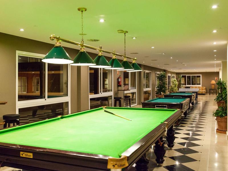 Ein heller Freizeitraum mit zwei grünen Billardtischen und modernen Pendelleuchten.