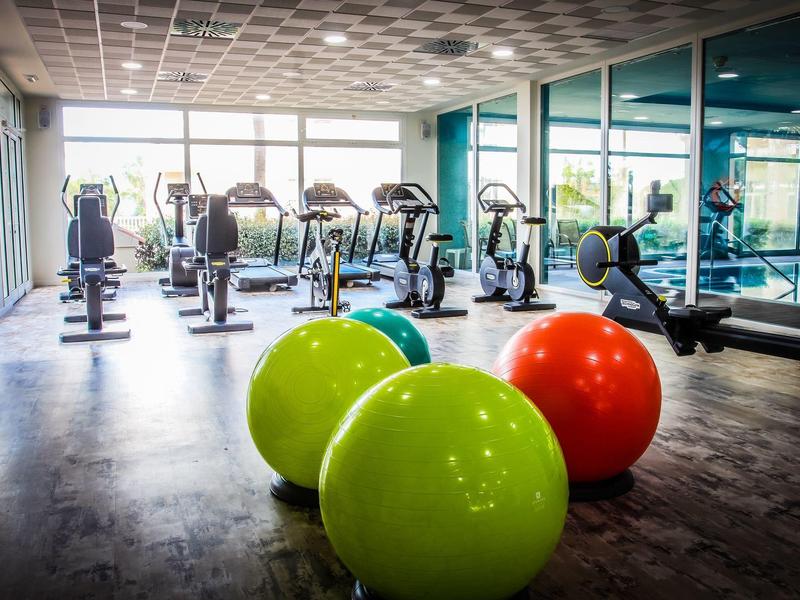 Helles Fitnessstudio mit großen Fenstern, Cardiogeräten und bunten Gymnastikbällen.