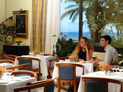 Gemütliches Restaurant mit weißen Tischen, blauen Stühlen, Pflanzen und Meerblick.