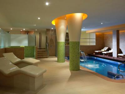 Moderner Wellnessbereich mit Pool, bequemen Liegen, warmem Licht und grün-beigen Säulen.