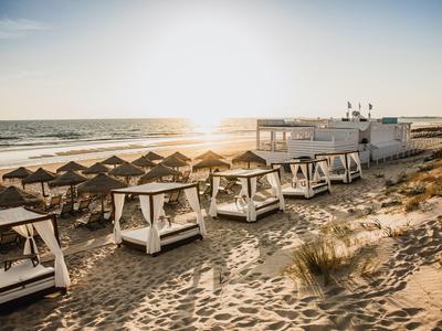 Strand mit Liegen, Sonnenschirmen und einem weißen Strandhaus im Sonnenuntergang.