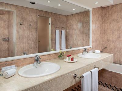 Helles Badezimmer mit großen Spiegeln, zwei Waschbecken, beiger Arbeitsplatte und Handtüchern.