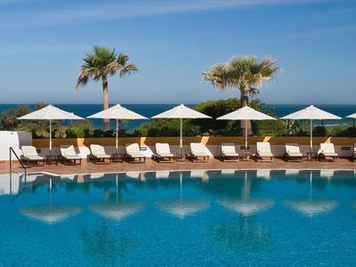 Schwimmbad am Meer mit Liegestühlen und Sonnenschirmen an einem sonnigen Tag.