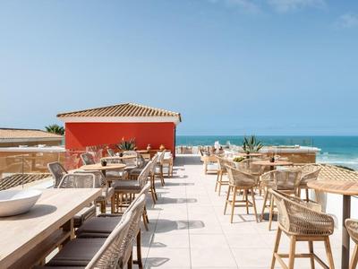 Terrassenrestaurant am Meer mit Holztischen, Stühlen und blauem Himmel.