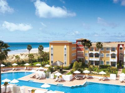 Großes Hotel mit Swimmingpools, Palmen und direktem Zugang zum Strand unter blauem Himmel.