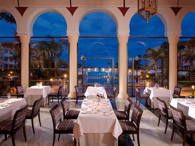 Elegantes Restaurant mit weißen Tischtüchern und Blick auf Pool und Garten bei Dämmerung