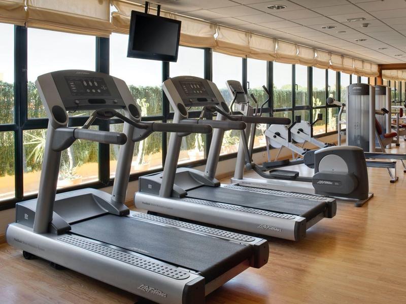 Moderner Fitnessraum mit Holzfußboden, drei Laufbändern, großem Fenster und Trainingsgeräten.