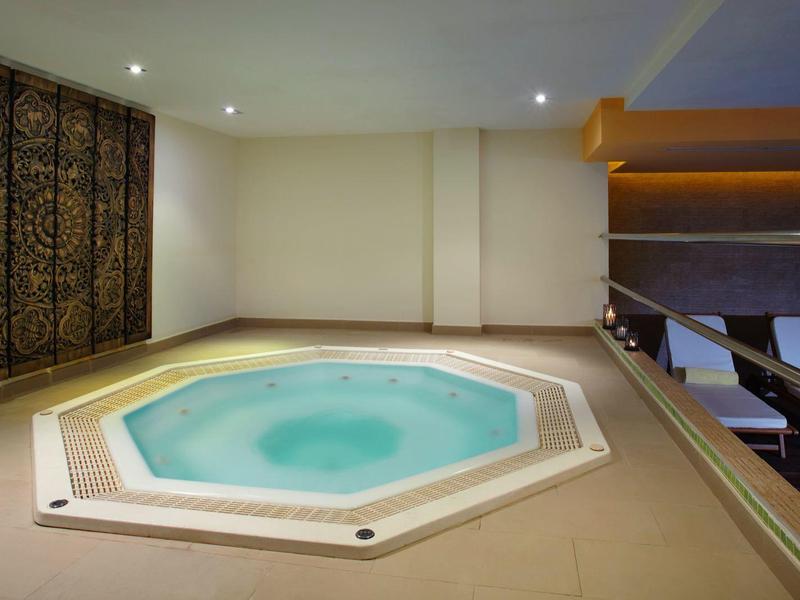 Moderner Whirlpool in hellem Raum mit gemusterter Wand und Holzverkleidung, daneben Liegestühle.