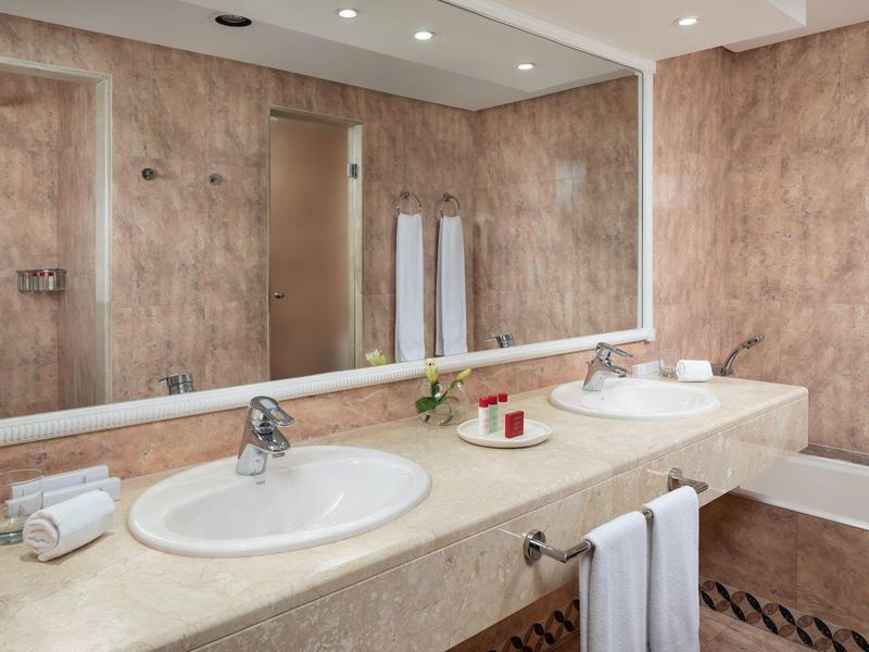 Helles Badezimmer mit großen Spiegeln, zwei Waschbecken, beiger Arbeitsplatte und Handtüchern.