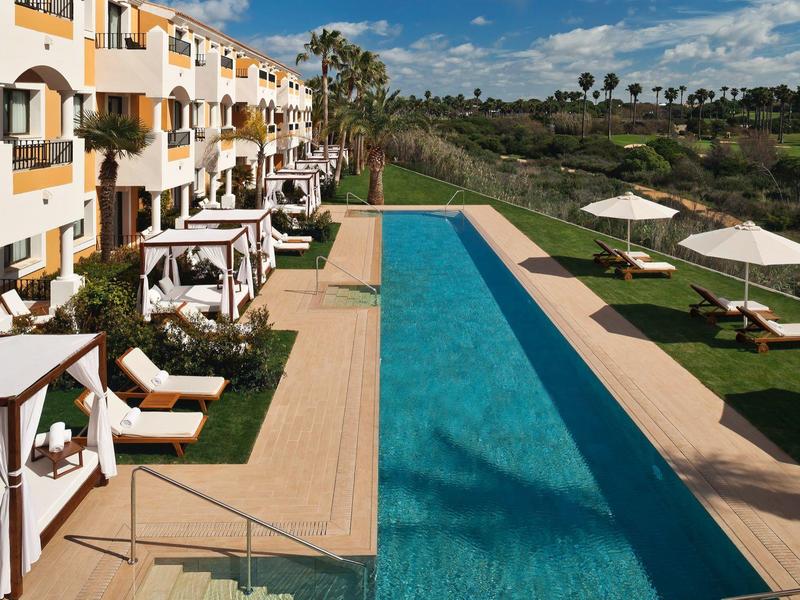 Moderner Außenpool mit Liegestühlen und Sonnenschirmen neben einem Mehrfamilienhaus.