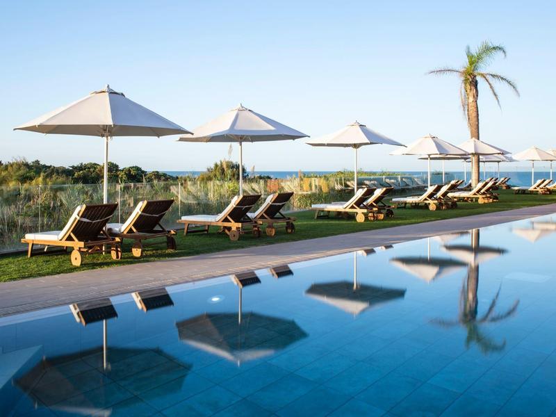 Einladender Pool mit Liegestühlen und Sonnenschirmen, klarem Wasser und blauem Himmel.