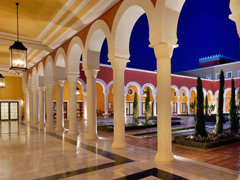 Abendliche Arkaden mit weißen Säulen, gelben Wänden und einem blauen Himmel im Innenhof.
