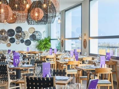 Modernes Restaurant mit großen Fenstern, Holztischen, schwarzen Stühlen und dekorativen Wandplatten.