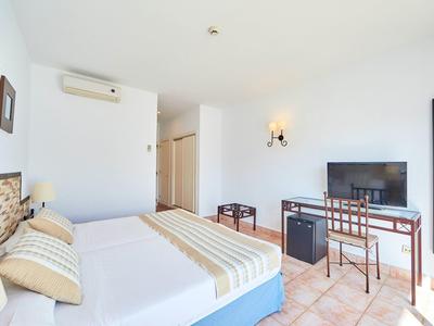 Helles Schlafzimmer mit Doppelbett, TV, Schreibtisch und Klimaanlage, weiße Wände und Terrakottaboden.