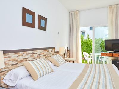 Hell eingerichtetes Schlafzimmer mit Doppelbett, weißen Wänden, Gardinen und Terrasse mit Gartenblick.