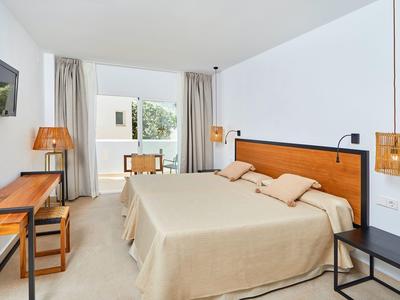 Schlichtes Hotelzimmer mit Doppellbett, Holzmöbeln, neutralen Vorhängen und großem Fenster.
