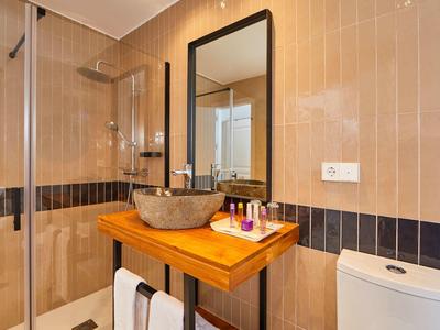Modernes Badezimmer mit braunen Fliesen, Glasdusche, Holzwaschtisch und ovalem Steinwaschbecken.