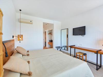 Helles Schlafzimmer mit Doppelbett, Holzmöbeln, Wand-TV und offenem Kleiderschrank in weißem Raum.