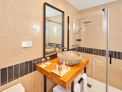 Moderner Badezimmer mit beige-schwarzen Fliesen, Glasdusche, Holztisch und rundem Steinwaschbecken.