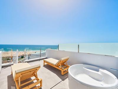 Terrasse mit zwei Holzliegen und einem weißen runden Whirlpool, Blick auf Strand und Meer.