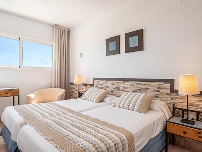 Helles Schlafzimmer mit Doppelbett, gestreiften Kissen, zwei Nachttischen und zwei Bildern an der Wand.